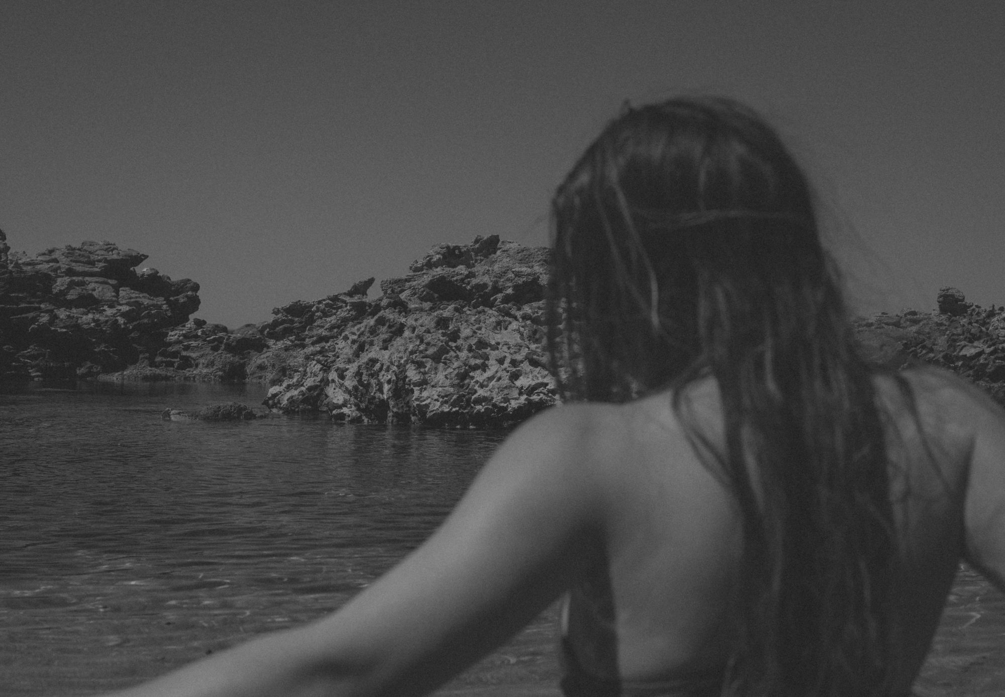 Black and white photo of a woman with long wet hair looking out over a rock pool and limestone rocks