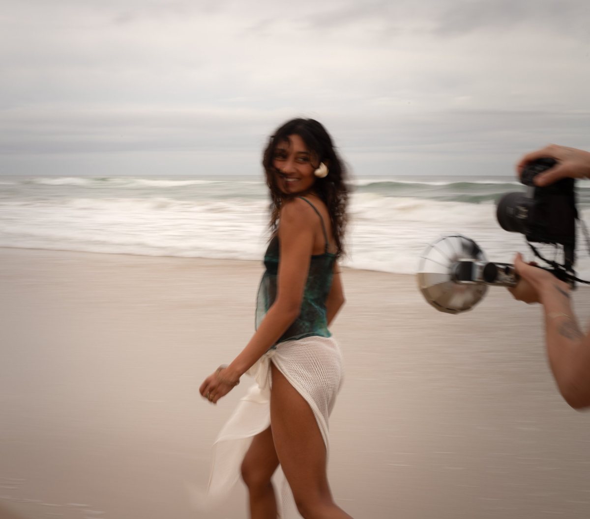 A woman glancing back over her shoulder as she walks the beach, with a photographer's camera and flash entering the frame