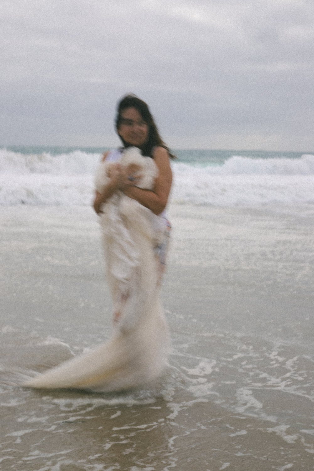 A softly blurred portrait of a woman holding lace to her chest as she stands in the shallows